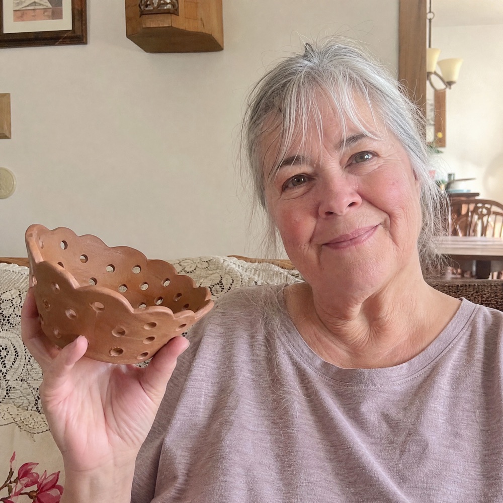 Karen M. holding her handmade ceramic piece at home